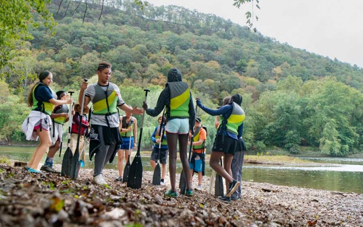 a group of teens stand on a shore on a canoeing expedition near baltimore